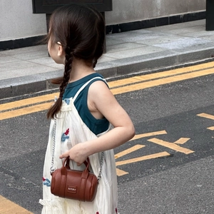 Close-up of children brown lychee leather cylinder bag with silver metal chain and logo