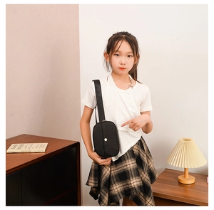 Close-up of a black canvas crossbody bag for kids with a round gold buckle detail