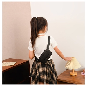 Rear view of a child wearing a black mini nylon crossbody bag over a white t-shirt