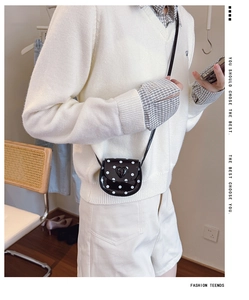 Close-up of a mini black and white polka dot crossbody bag with a 3D heart buckle detail