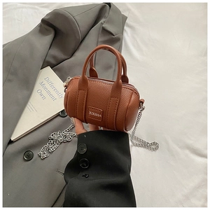 Detail of a brown leather mini cylinder bag with litchi texture and silver chain strap