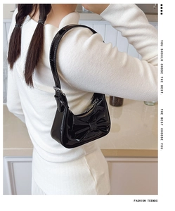 Close-up of black glossy patent leather shoulder bag with a stylish bow decoration