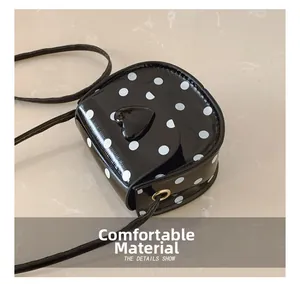 Close-up of black polka dot girl bag with heart-shaped buckle and glossy texture