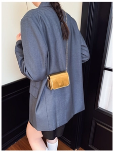 Close-up of a mini golden mirror crossbody bag with a slim metal chain strap on a model