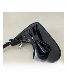Close-up of a black patent leather handbag featuring a large bow and silver metal zipper
