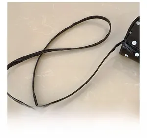 Close-up detail of the slim shoulder strap and white polka dot pattern on black purse