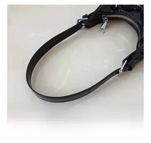 Close-up of black glossy patent leather bag showing silver metal zipper and buckle details