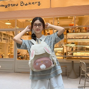 Japanese style cream backpack with cute rabbit ears and plush ball in a bakery setting