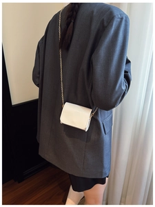 Rear view of a model wearing a mini white patent leather flap bag with gold chain strap