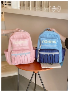 Detail of colorful nylon school backpacks with YXCHTOG lettering on a wooden table