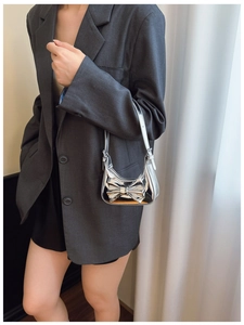 Detail of silver laser mirror handbag with 3D bow on grey blazer background