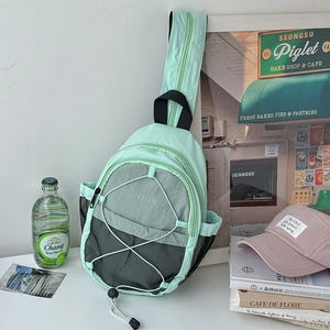 Detail of mint green and grey nylon chest bag featuring a front bungee cord system