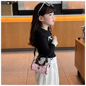 Détail du sac cylindre rose avec nœuds et breloque cœur porté par une fille