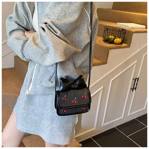 Mini sac bandoulière pour fille avec grand nœud et broderie cerise porté par un mannequin