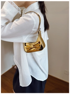 Detail of a shiny gold metallic shoulder bag with a large bow worn by a child model