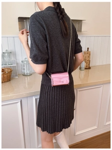 Pink laser glossy patent leather mini chain bag for kids worn by model in home setting