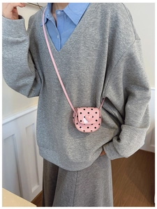 Close-up of pink polka dot mini crossbody bag with a heart charm worn by a child