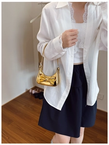 Close-up of metallic gold mini handbag featuring a decorative bow on white shirt outfit
