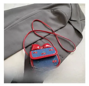 Close-up of cherry embroidery and red leather bow detail on blue denim crossbody bag
