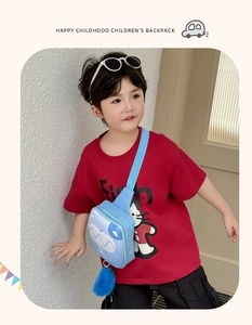 Detail of blue shark kids chest bag with plush ball charm worn by a child in red