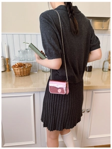 Detail of pink metallic crossbody bag with gold chain strap on a model in a cafe
