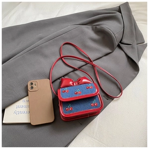 Détail du mini sac bandoulière avec broderie cerise et décoration nœud rouge
