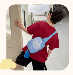 Detail of blue kids chest bag with cartoon monster print and fuzzy tail charm