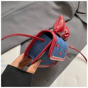 Détail du mini sac bandoulière en denim avec broderie cerise et grand nœud rouge