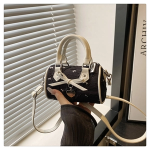 Détail du sac barillet noir texturé avec nœud blanc et breloque en forme de cœur doré