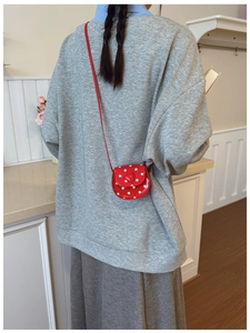 Detail of red polka dot mini crossbody bag with heart motif worn over a grey hoodie