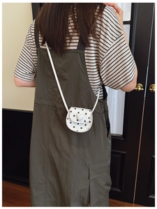 Detail of a mini white crossbody bag with black polka dots and a heart buckle for girls