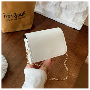 Close-up of white patent leather mini bag with gold chain strap held by hand