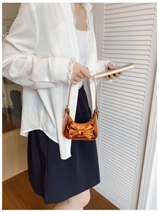 Detailed view of kids' metallic orange bow handbag worn by a child model outdoors