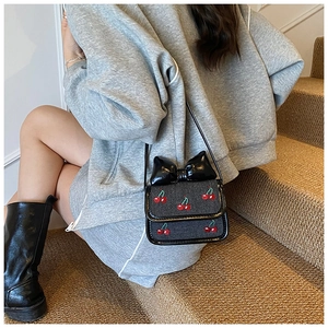 Détail d'un mini sac bandoulière noir avec broderie cerise et un grand nœud décoratif