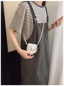 Close-up of a mini white polka dot crossbody bag with a heart buckle worn by a child