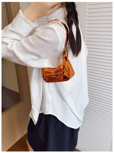 Detail of orange metallic laser mirror handbag with large bow carried by a young model
