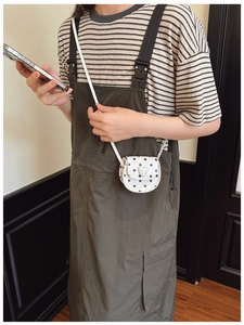 Detailed view of mini white polka dot crossbody bag with heart buckle on striped outfit