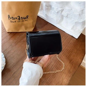 Detail of a mini glossy black patent leather chain bag with fine gold metal strap