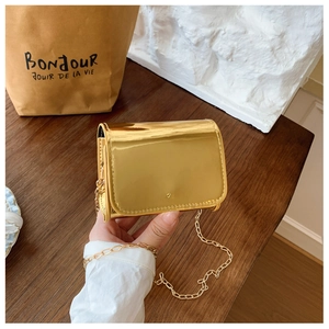 Detail of a mini gold metallic crossbody bag with fine chain strap and glossy finish