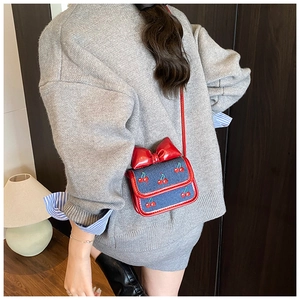 Detailed view of kids' blue knit crossbody bag with red bow and cherry embroidery