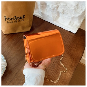 Detail of a shiny orange mirror-finish mini crossbody bag with a slim gold chain strap