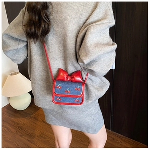 Détail du nœud rouge et broderie cerise sur un mini sac à bandoulière en denim