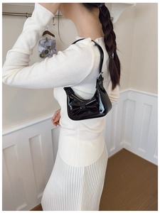 Side view of a glossy black bow handbag being worn by a child in a minimalist room