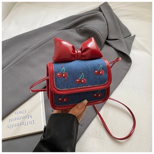 Détail d'un sac bandoulière en denim avec grand nœud rouge et motif cerise brodé