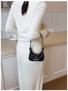 Glossy black patent leather bow bag worn with a white knit top and pleated skirt