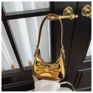 Detail of golden metallic crescent bag with bow hanging on a black wooden door handle