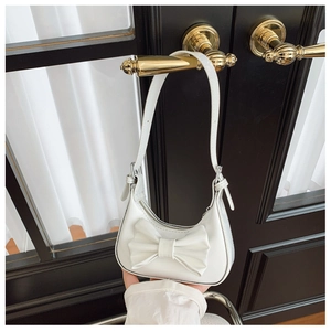 Detail of white half-moon bag with large bow hung on a door handle for elegant style