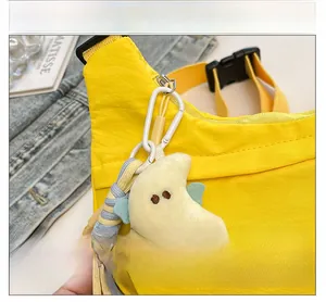 Detail of yellow nylon messenger bag featuring a plush moon charm with blue wings