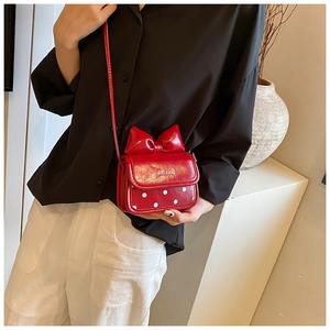 Detail of red bow crossbody bag with white polka dots and glossy finish on model
