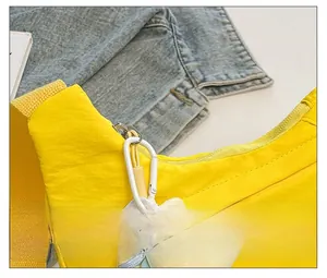 Detail of yellow nylon sling bag showing smooth metal zipper and plush animal charm